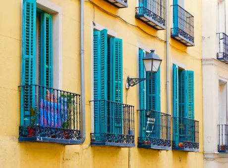 tiny balconies vivid blue shutters vibrant yellow wall lavapies district downtown madrid spain