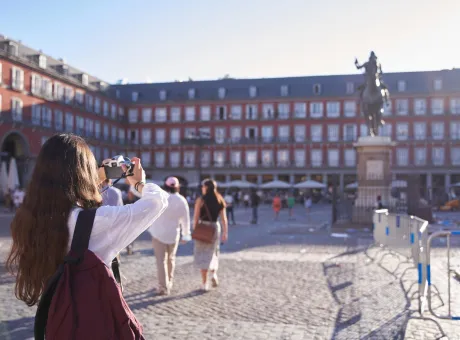 young tourist holding camera taking photo plaza mayor madrid spain tourist attraction 16th century statue philip iii background